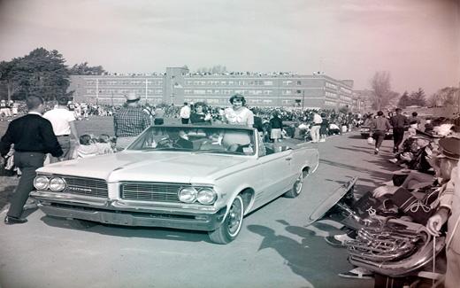 Following the 1962 Football Game, the Homecoming Queen is driven away in a convertible.