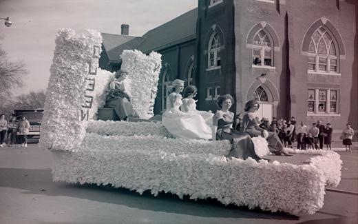 西北塔女王, 穿着她的晚礼服, rides on a float with her royal court during the 1962 Homecoming Parade.